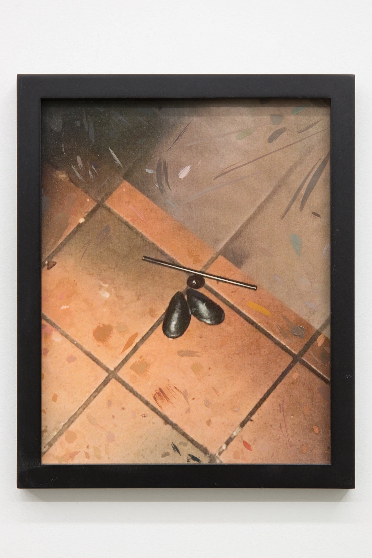 Detail image of a printed photograph framed in a thin matte black frame. The printed image has small marks of oil paint. The image is of a single splayed out mussel, one blueberry, and a plastic straw on top of saltillo tiles and next to a stainless steel refrigerator.