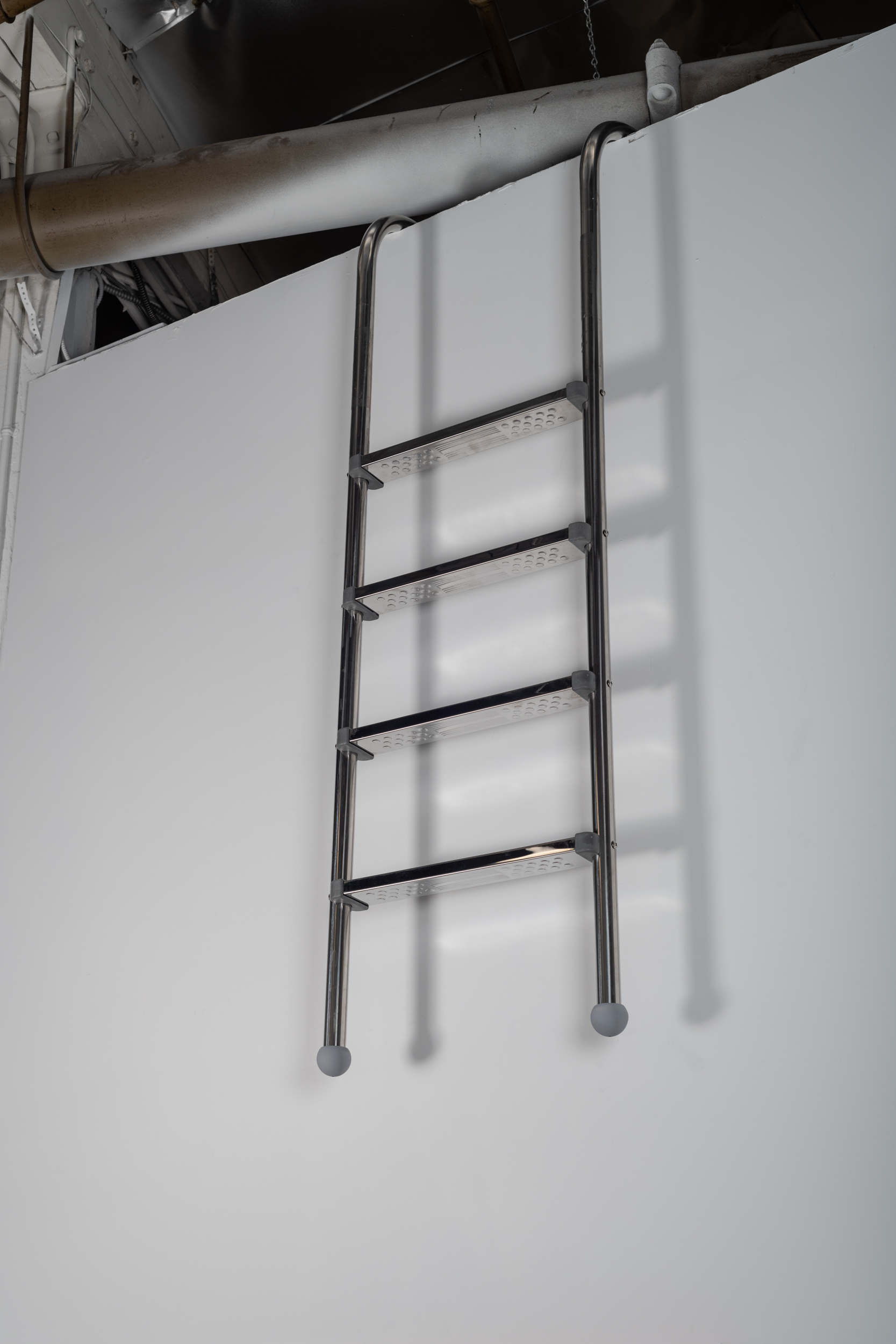 This image is a close up of an aluminum pool ladder which curves over the top of the wall–leading to nowhere.